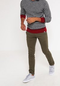 Strickpullover mit Schwarz-Weiß-Muster und roten Bündchen sowie Saum; olivgrüne Slim-Fit-Hose; graue Sneakers.