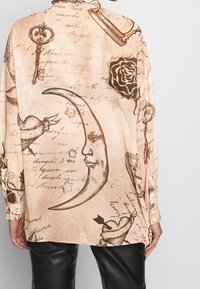 Camicia a maniche lunghe in morbido tessuto beige con disegni neri intricati di chiavi, luna, stelle, rosa e scritte; vestibilità comoda e chiusura con bottoni.