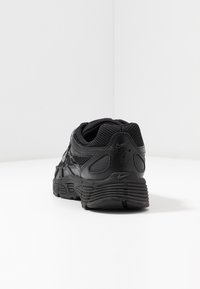 Czarne buty sportowe z cholewką z siateczki i materiałów syntetycznych, zaokrąglonym czubkiem, teksturowaną podeszwą i wyraźnym logo Nike na pięcie, widziane od tyłu.