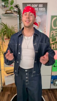 Jeansjacka med silverknappar och mörkblå färg, parat med en vit linne och matchande jeansbyxor med knappdetaljer. Röd bandana som accent.