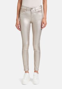 Jeans ajustados de color dorado metálico con una textura suave, cinco bolsillos y cierre de botón. Combinados con zapatillas deportivas de plataforma blancas.
