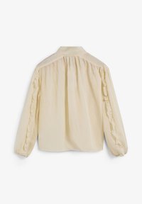 Camisa de crema clara con un cuello simple, mangas largas con acentos de volantes y un corte holgado. Tejido texturizado con un aspecto suave y ligero.