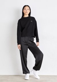 Sweat-shirt noir court à encolure ronde avec logo brodé, associé à un pantalon noir ample et des baskets blanches. Tissu lisse, coupe décontractée.