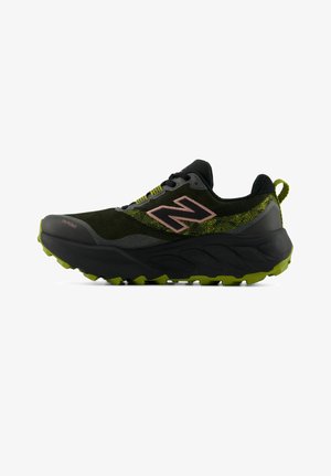 Chaussure de trail noire et verte avec une semelle épaisse, une bande de roulement robuste, et un logo New Balance rose sur le côté.