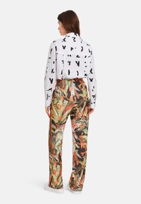 Witte shirt met zwarte grafische patronen, gecombineerd met meerkleurige broek met een jungleprint en oranje zijkanten. Casual schoenen.