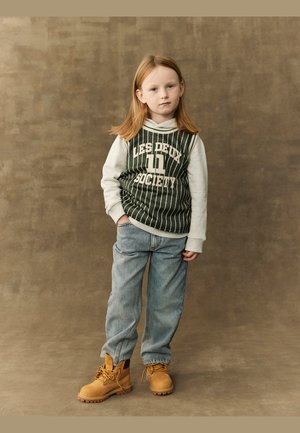 Grønnstripet hettegenser med grå ermer, med tekst. Lyseblå jeans og brune boots med snøring. Enkelt brunt bakgrunn.