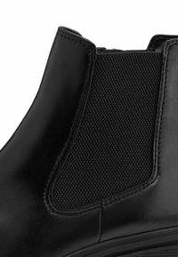 Bottine en cuir noir avec un panneau latéral élastique texturé, des coutures décoratives et un bout arrondi avec une semelle basse.