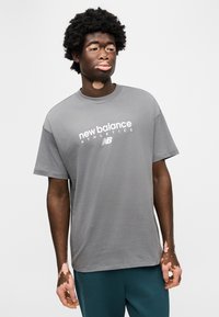 Γκρι βαμβακερό μπλουζάκι με στρογγυλή λαιμόκοψη και κοντά μανίκια, με λευκό λογότυπο "new balance" στο στήθος.