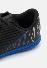 Schwarzer Sportschuh mit horizontalen Linien, blauer Sohle und auffälliger weißer Markenkennzeichnung. Leichter Mesh-Oberstoff mit strukturiertem Finish.