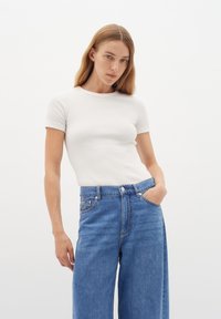 T-shirt bianco a coste con maniche corte abbinata a jeans larghi a vita alta blu. Materiale in cotone con una texture liscia e design classico.