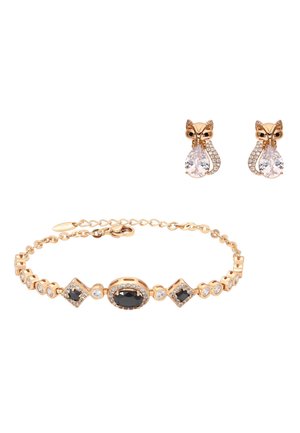 Gouden armband met zwarte en heldere edelstenen naast gouden oorbellen in de vorm van een vos, met druppelvormige kristallen.