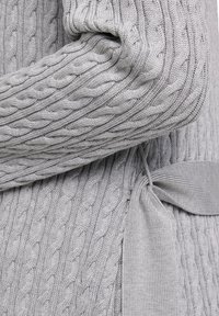 Grau gestrickter Pullover aus Kabelstrick mit strukturiertem Muster, lockerer Passform und einem gebundenen Taillengürtel für eine anpassbare Styling-Option.