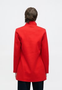 Red wool coat with a high collar, tailored fit, and long sleeves, featuring a smooth texture and clean lines, viewed from the back.
