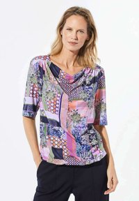 Bunte Bluse mit drapiertem Ausschnitt, kurzen Ärmeln und verschiedenen Mustern, einschließlich Blumen- und geometrischen Designs auf einem glatten Stoff.