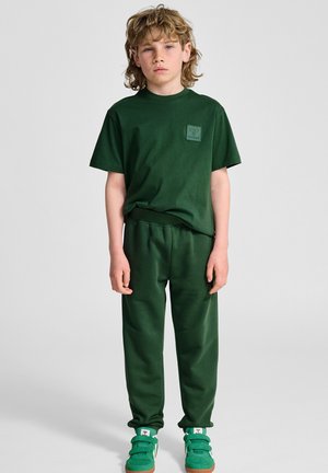 Groene katoenen t-shirt en bijpassende sweatpants, met een klein logo-opdruk op de borst, gecombineerd met groene sneakers. Soepele textuur, ontspannen pasvorm.