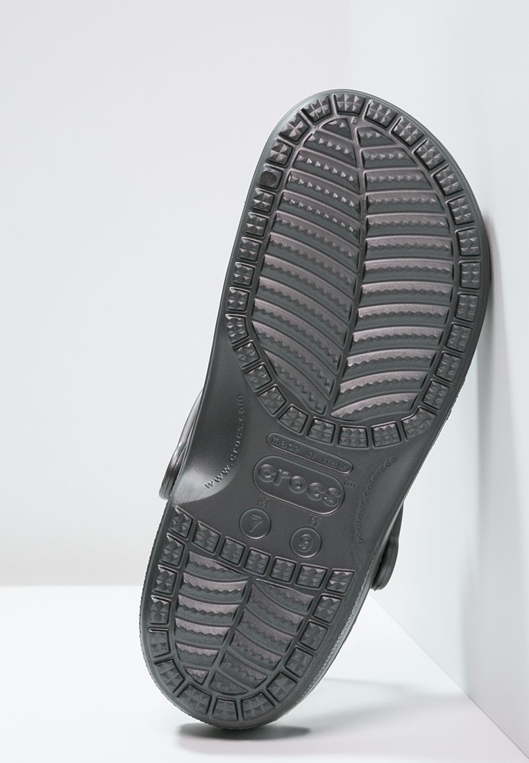 Zwarte rubberen schoen met een gevormde voetbed en een getextureerde zool. Bevat afwateringsgaten en een achterriem voor een veilige pasvorm.