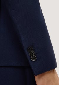 Ärmel eines navyblauen Anzugs aus strukturiertem Stoff, mit drei schwarzen Knöpfen im kreisförmigen Design und einem klaren Abschluss am Ärmel.