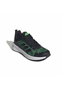 Chaussure de sport noire avec un motif Minecraft vert, empeigne en mesh, trois bandes noires et une semelle en caoutchouc texturée.