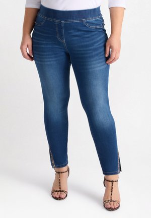 Vaqueros ajustados de denim azul que cuentan con una cinturilla elástica alta, acentos de abertura lateral y una textura suave. Combinados con tacones de estampado animal.