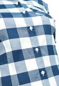 Modrá a bílá kostkovaná košile vyrobená z bavlny, s knoflíkovou přední částí, čtyřmi knoflíky a vyšitým kapsou na levé straně.