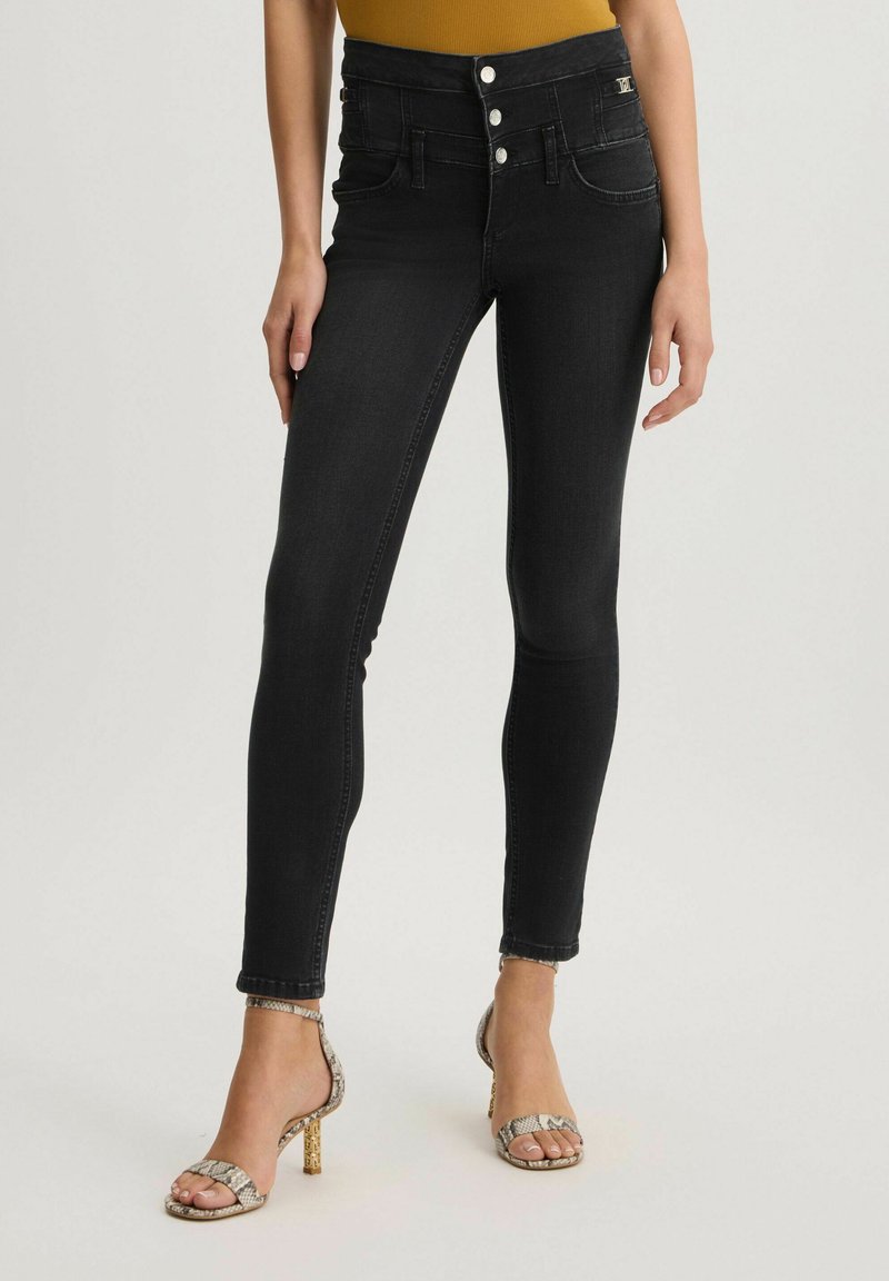 Jeans skinny neri a vita alta con chiusura a cinque bottoni, tasche frontali e dettagli di cucitura sottile. Abbinati a décolleté in stampa pitone.