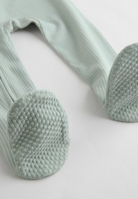 Světle mákově zelené legíny s ribovanou texturou, které mají strukturovanou protiskluzovou podrážku pro lepší grip. Materiál vypadá měkce a pružně.