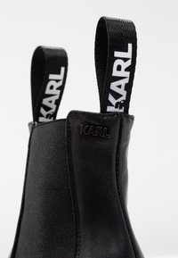 Black ankle boot featuring a smooth leather exterior, elastic side panels, and prominent black and white KARL branding on the pull tabs.
