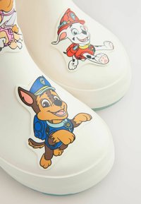 Bottes de pluie blanches en caoutchouc ornées de motifs de dessins animés représentant un chien brun et bleu en uniforme de police et un chien blanc avec un chapeau rouge.