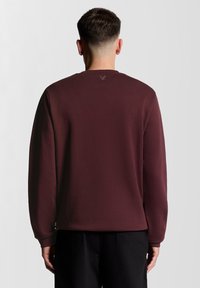 Βουργουνδί φούτερ με στρογγυλή λαιμόκοψη από απαλό ύφασμα, με μακριά μανίκια, ριμπ τελειώματα στα μανίκια και ένα μικρό λογότυπο στην πίσω πλευρά του λαιμού.