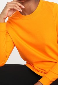 Helles orange Sweatshirt aus Baumwolle, mit einem runden Ausschnitt, langen Ärmeln und einer lockeren Passform, mit einer glatten Textur.