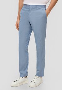 Helles blaues, maßgeschneidertes Hosenmodell aus atmungsaktivem Material, mit einem dezenten Karomuster, slim fit und Seitentaschen. Getragen mit weißen Sneakers.