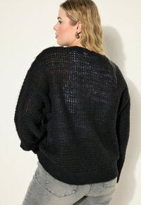 Schwarzer gestrickter Pullover mit lockerer Passform, strukturiertem Gewebe und geripptem Saum. Der Rücken zeigt ein dezentes Muster und lange Ärmel.