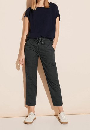 Granatowa bluzka z krótkim rękawem w połączeniu z ciemnoszarymi spodniami bojówkami z troczkiem w talii. Noszone z białymi tenisówkami, na tle o neutralnym kolorze.