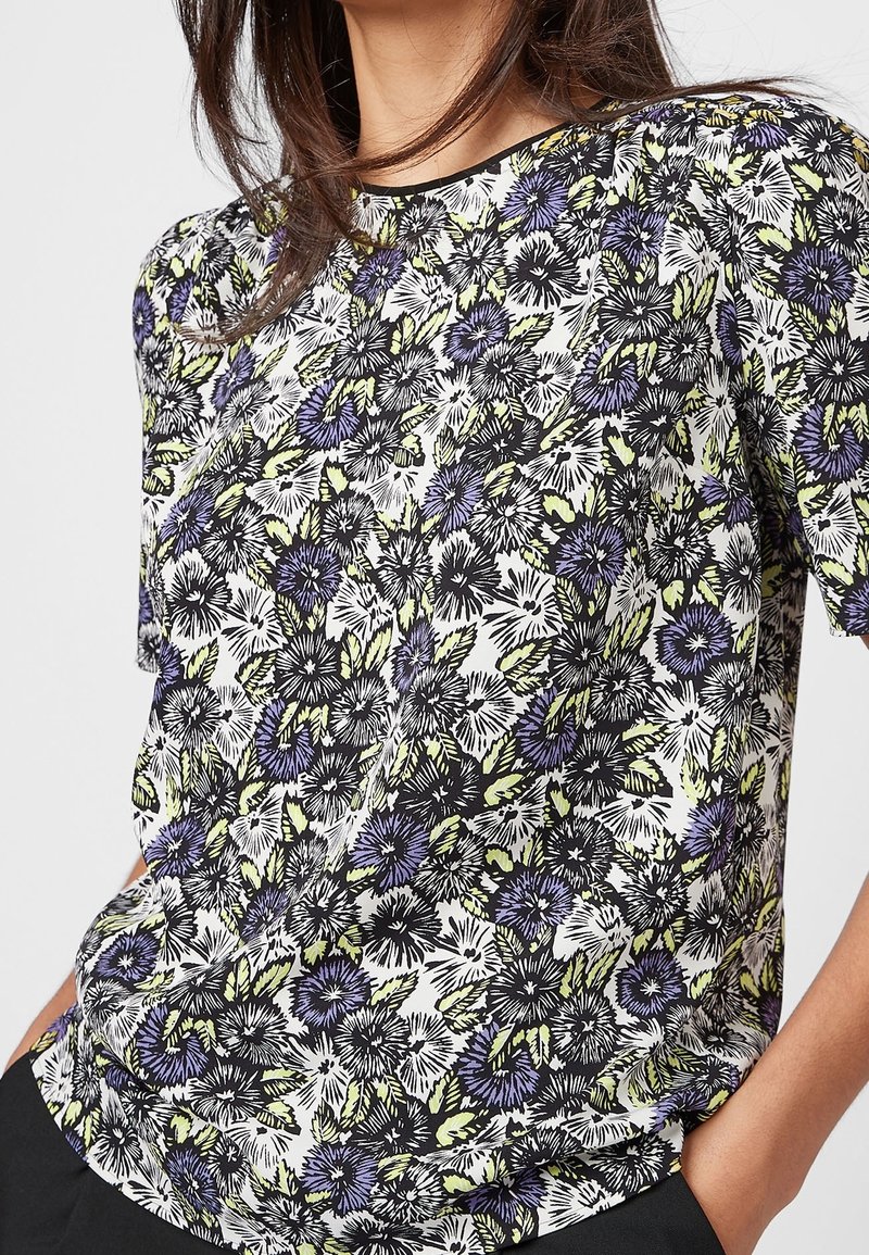 Korte mouw bloemen top met een witte achtergrond en paarse en groene bloemenpatronen, gemaakt van lichtgewicht stof met een ontspannen pasvorm.