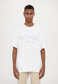 Baltos medvilnės marškinėliai su per dideliu siluetu, apvaliu iškirpimu ir mėlynai spaudinta užrašu "Just Gavalli Milano" priekyje. Trumpomis rankovėmis.