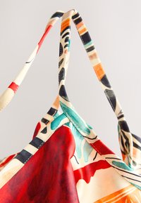 Fabric bag handles in close-up with colorful abstract patterns in red, teal, orange, black, and cream tones.