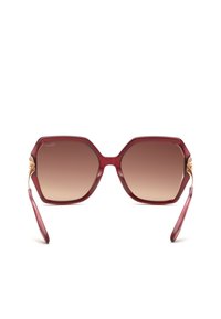 Lunettes de soleil hexagonales rouges surdimensionnées avec des verres marron dégradés et des charnières décoratives dorées sur fond blanc.