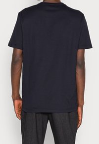 Námořnicky modré bavlněné tričko s klasickým kulatým výstřihem, krátkými rukávy a hladkou strukturou. Obsahuje rovný lem a minimalistický design.
