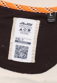 T-shirt merklabel van J&Joy, met een zwarte basis en een beige stof met een oranje geweven accent. Bevat een QR-code en wasinstructies.