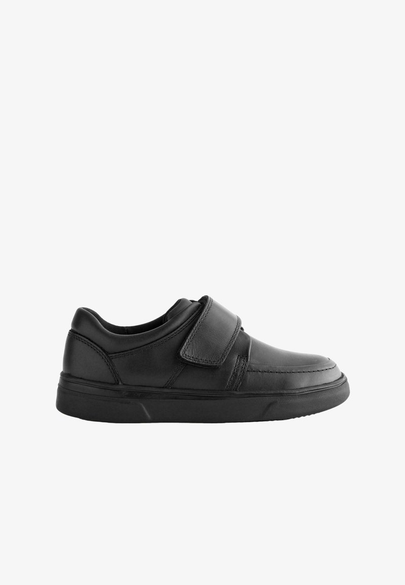 Chaussure décontractée en cuir noir avec une large sangle Velcro, un col rembourré et une semelle épaisse en caoutchouc, vue de côté sur fond blanc.