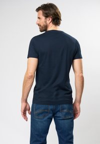 Tumesinine lühikeste varrukatega T-särk, mis on valmistatud puuvillast, ümmarguse kaelusega ja mugava lõikega, koos siniste teksadega, millel on tavalised tagakotid.