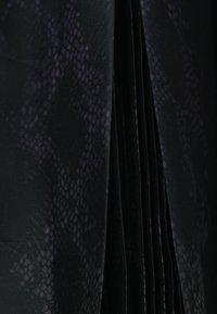 Zwart geplooid stof met een gestructureerd patroon dat lijkt op dat van een reptiel, met subtiele paarse ondertonen, wat zorgt voor visuele diepte en contrast.