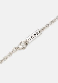 Pulseira de corrente de prata com uma etiqueta plana gravada com "ICON" e um fecho tipo lagosta. A corrente tem uma textura lisa e polida.