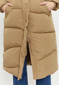Puffer coat in light brown with quilted design, high collar, zip closure, and side pockets. Smooth texture with a slightly glossy finish.