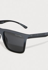 Ochelari de soare dreptunghiulari negri cu un finisaj mat, lentile gri și text embosat "Armani Exchange" pe brate. Material plastic rezistent.