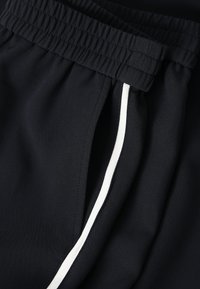 Shorts de sport bleu marine avec une taille élastique, présentant des bandes blanches sur les côtés et un tissu lisse et léger.