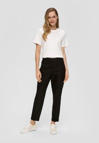 T-shirt blanc avec de légères rayures horizontales, associé à un pantalon noir sur mesure. Le modèle porte des baskets crème ; design simple, sans motifs visibles.