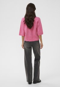 Weit geschnittener rosa Pullover mit kurzen Ärmeln, geripptem Saum, kombiniert mit hoch taillierter grauer Jeans und schwarzen Stiefeletten. Glatte Textur.