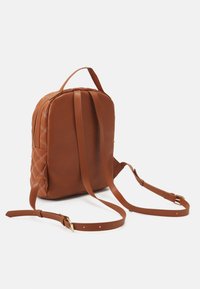 Mochila de imitación de cuero marrón con detalles laterales acolchados, correas ajustables y herrajes en tono dorado. Forma redondeada con asa superior.