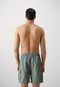 Heren cargo zwemshorts in lichtgroen, met een elastische tailleband en zijzakken. Het materiaal lijkt lichtgewicht met een gestructureerde afwerking.